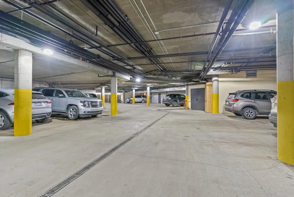 A practical, well-lit parking garage area with parked vehicles, yellow painted columns, and concrete flooring, offering a secure place to store your car and easily access your gear for any activity.