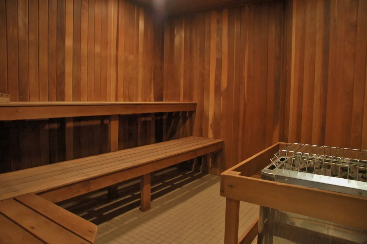 A tranquil sauna interior with wooden benches and a sauna heater offers a space for relaxation and detoxification. The inviting warmth of the wood and intimate size suggest a cozy spot to unwind after a day of activity.