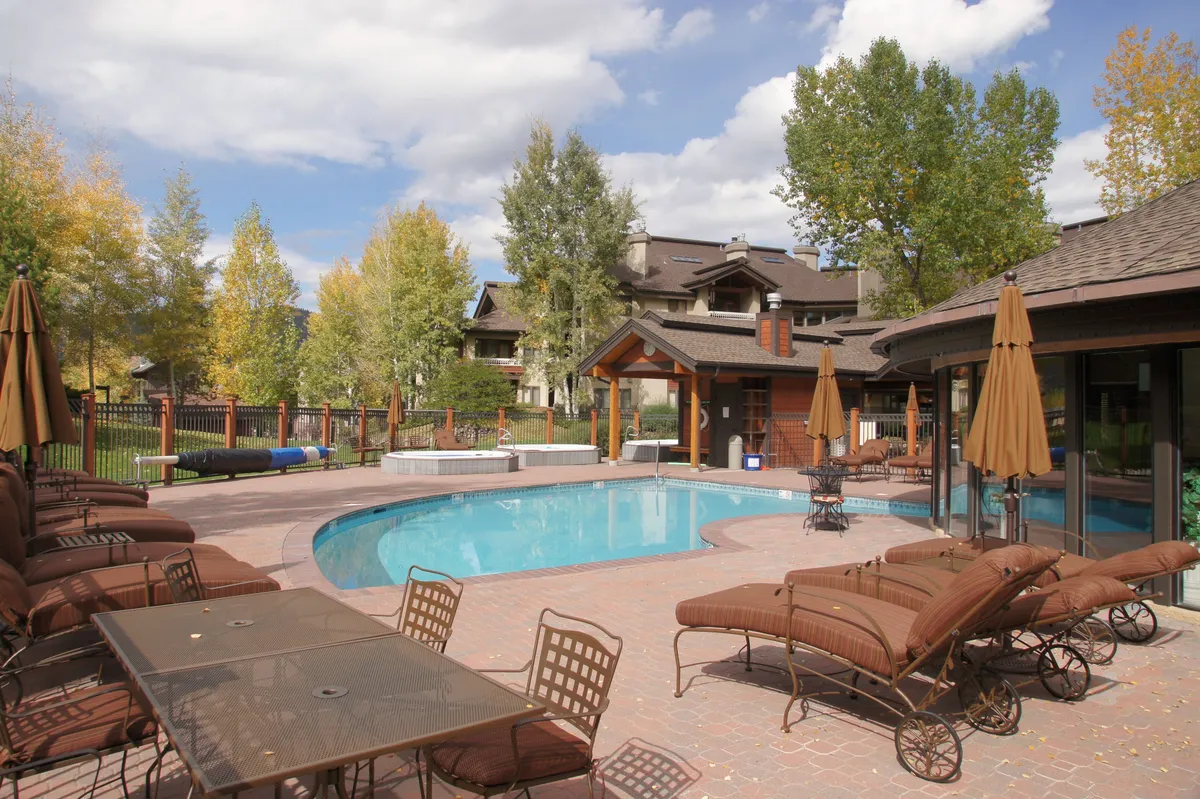 A sparkling swimming pool surrounded by lounge chairs and an outdoor dining table, all set amidst a peaceful grove of trees. The scene suggests relaxation, outdoor recreation, and socializing by the pool.