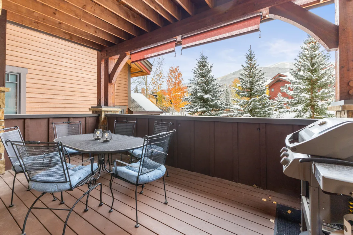An outdoor dining area featuring a table set for meals and a barbecue grill, surrounded by lush trees. The space offers a picturesque spot for enjoying the mountain air and dining al fresco in all seasons.