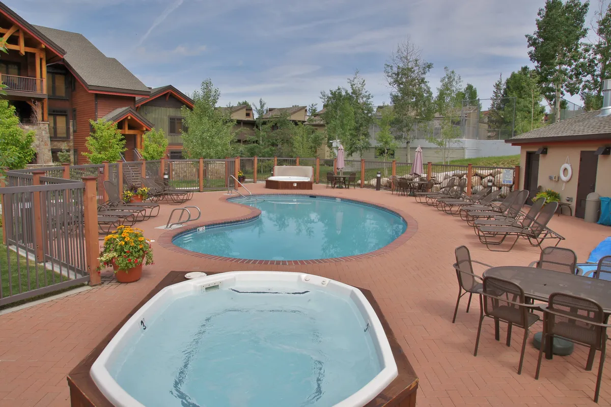 This inviting exterior shot shows a sparkling swimming pool surrounded by lounge chairs, a bubbling hot tub, and an outdoor dining area nestled in lush greenery. The relaxed layout encourages both sunbathing and socializing, while the pool and hot tub evoke a true resort atmosphere.