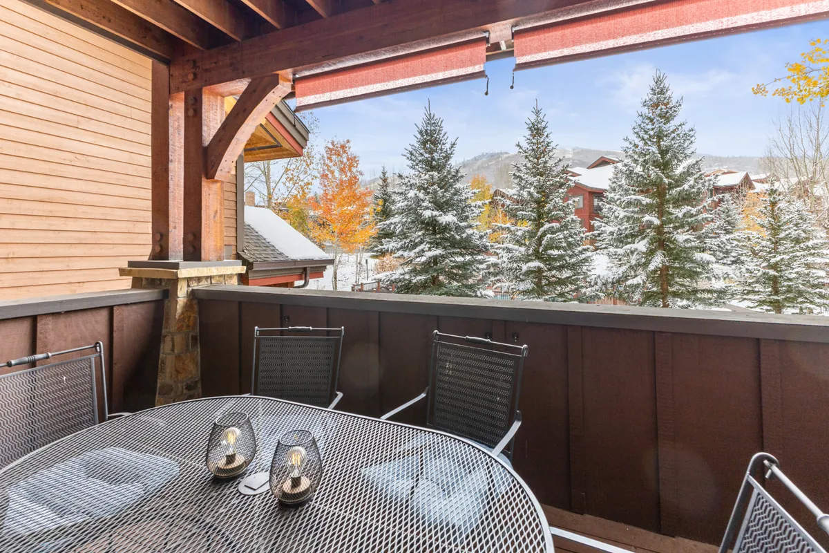 A serene covered deck with an outdoor dining table, surrounded by snow-covered trees and offering distant mountain views. The setting effortlessly blends indoor comfort with the fresh mountain air.