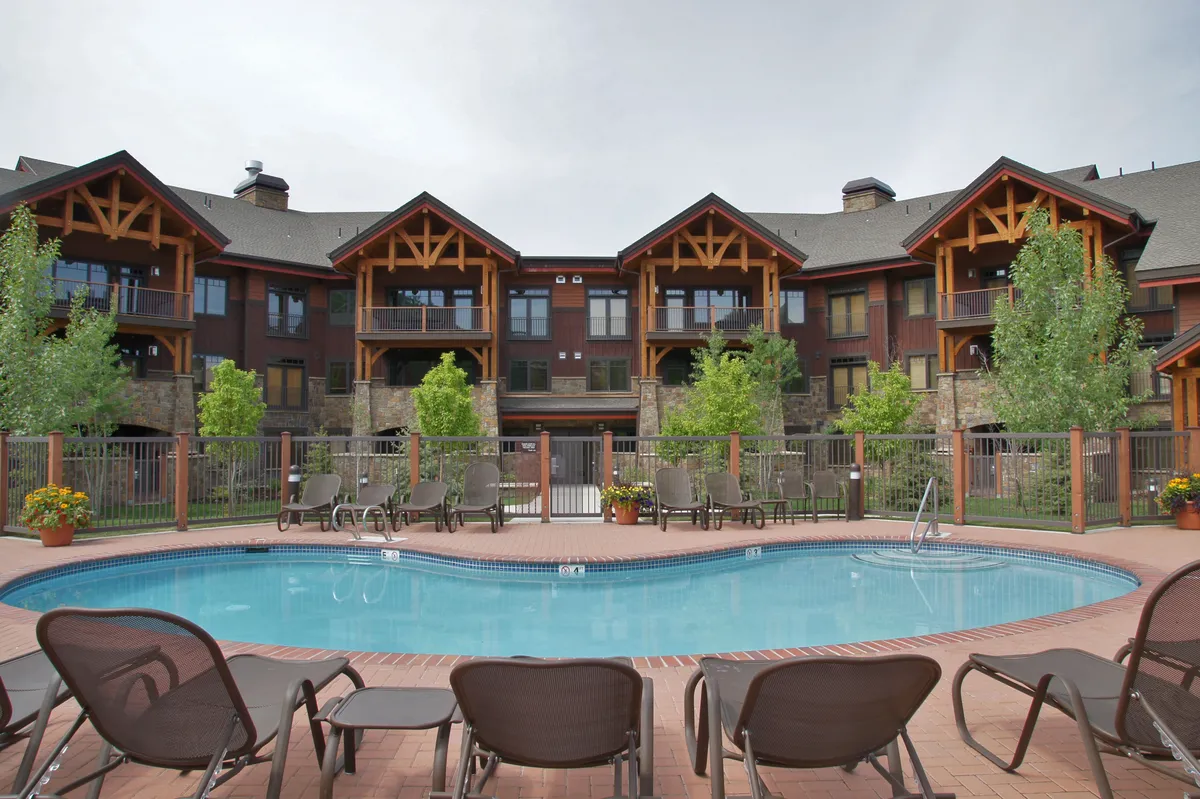 A large swimming pool sits center stage, lined with lounge chairs and bordered by lush landscaping and the building's inviting facade. The setting is relaxed and communal, hinting at both summer and winter fun for families.