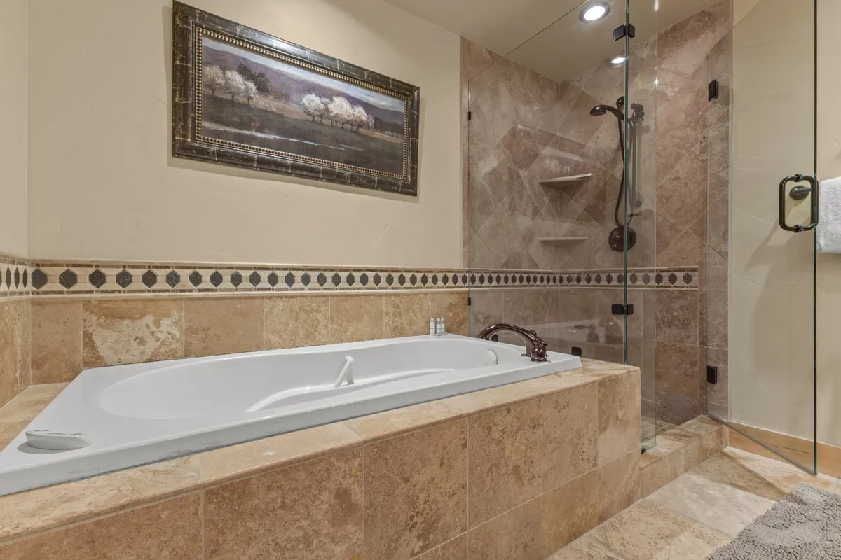 A spa-inspired bathroom featuring a jacuzzi tub, glass shower enclosure, and framed artwork. The atmosphere is tranquil, inviting guests to unwind in a luxurious setting after adventurous days.