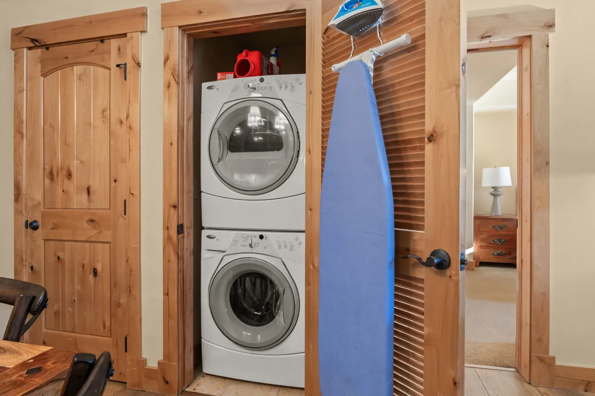 A practical and inviting laundry space featuring a stacked washer and dryer and an ironing board, seamlessly integrated into the home.