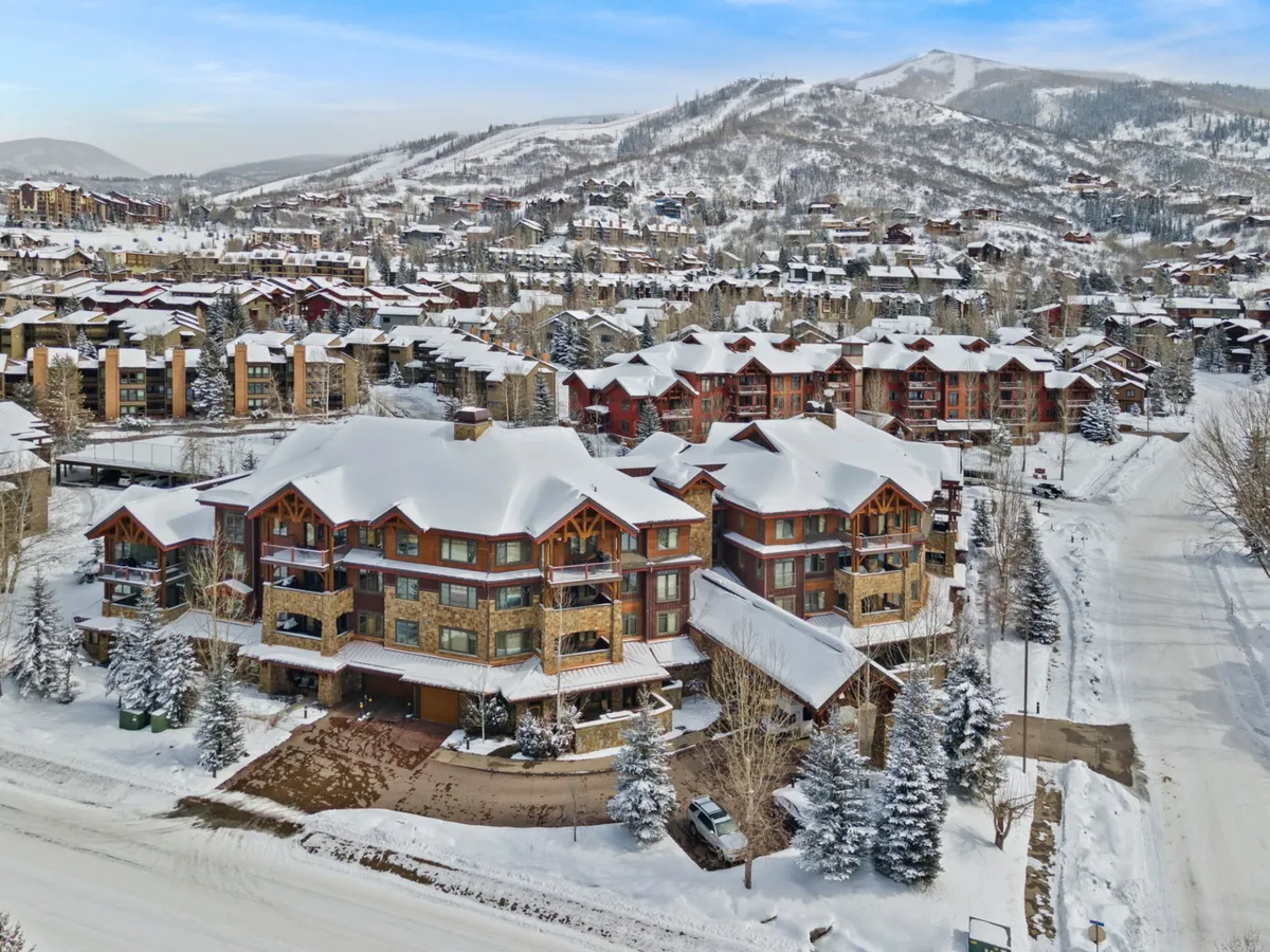 An exterior winter scene showcasing snow-covered buildings, a mountain backdrop, and tree-lined streets. The picturesque setting highlights the condo's proximity to Steamboat’s gondolas, trailheads, and village life.