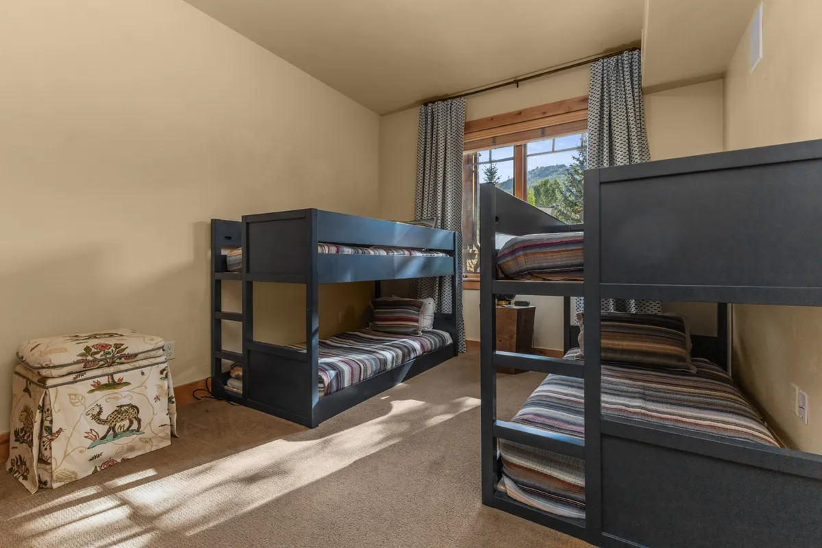 A cheerful bunk room with twin-over-twin bunk beds, a window letting in natural light, and a decorative ottoman at the foot of the beds. The space feels playful yet orderly, making it perfect for children or singles.
