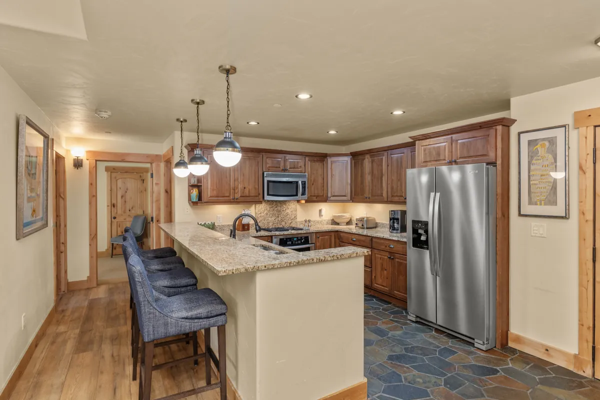 A modern, fully equipped kitchen with granite countertops, wooden cabinetry, stainless steel appliances, and a kitchen island with bar seating. The setup is ideal for preparing meals together and casual breakfasts.