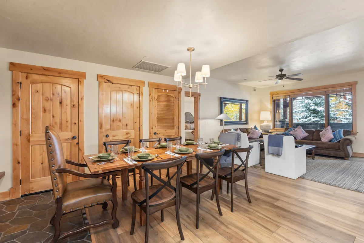 An open dining area seamlessly connects to a comfortable seating space, with a large dining table and charming wooden details. Expansive windows flood the room with daylight, creating a perfect spot for group meals and celebrations.