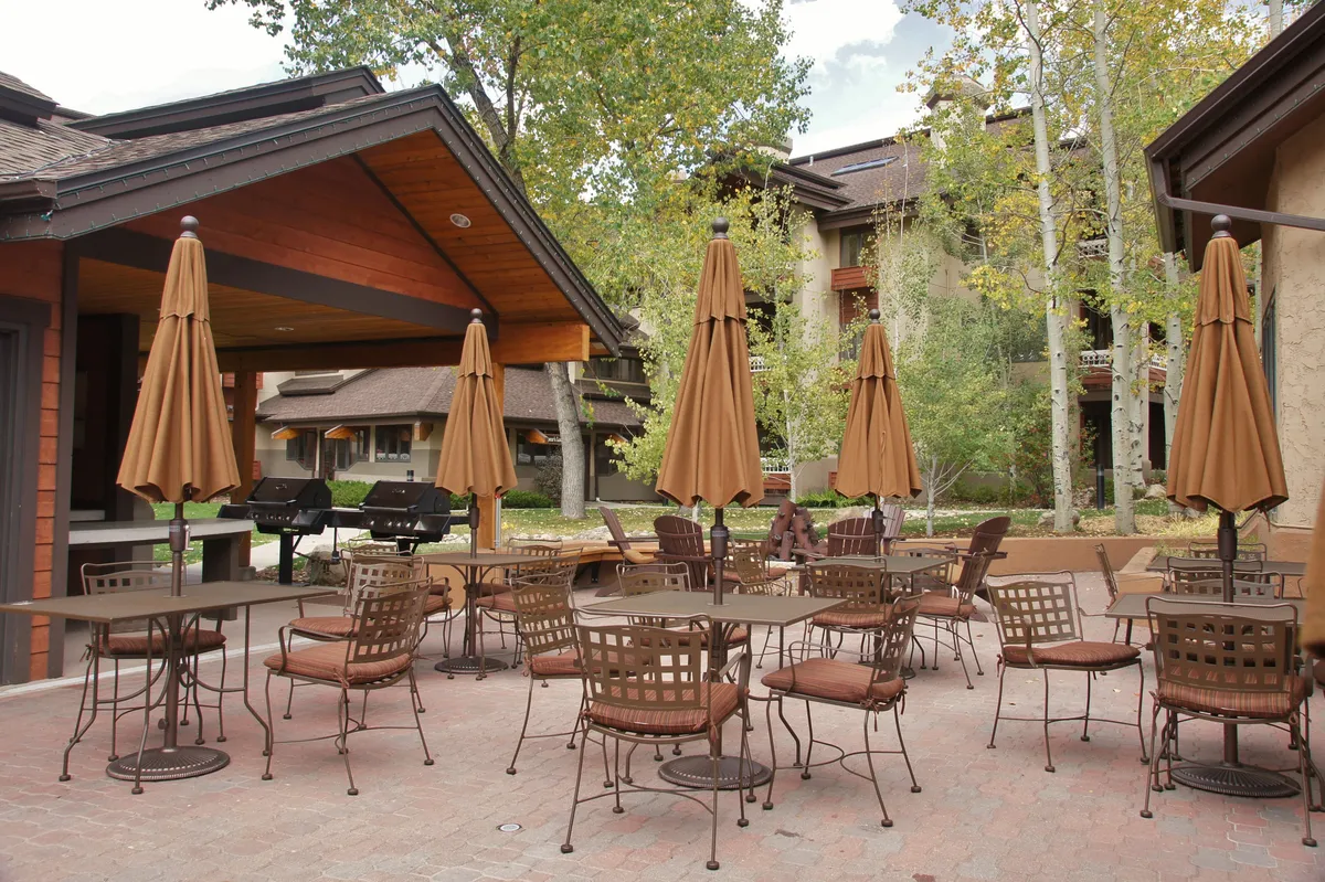This exterior image showcases a beautifully landscaped outdoor seating area with umbrellas, surrounded by greenery, perfect for socializing and relaxing. The area is lively yet inviting, suggesting a place for friends to gather after a day of mountain activities, enjoy live music events, or simply unwind with a drink while taking in sunset views.
