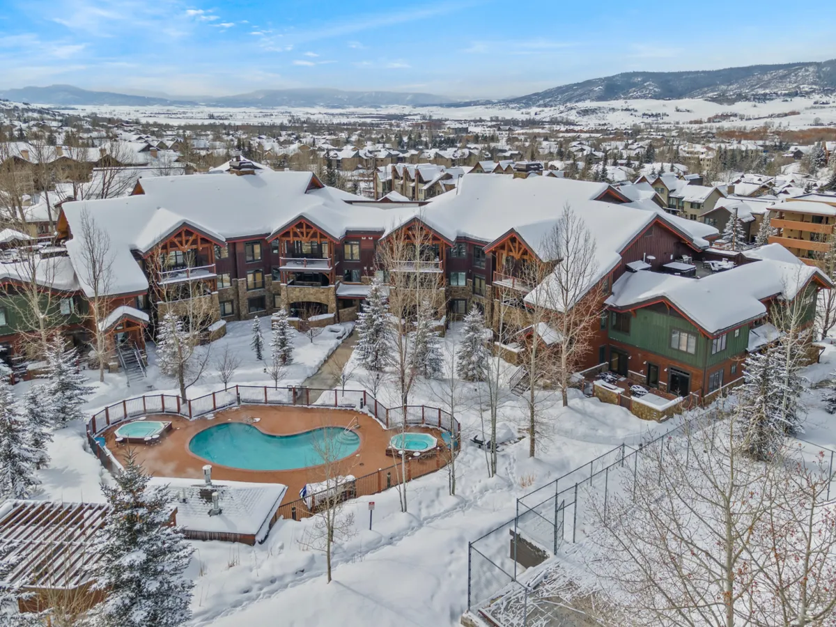 This image presents a picturesque winter scene with snow-covered buildings, an outdoor pool steaming in the cold air, snowy landscape, and surrounding mountains. The vibrant interplay between the inviting pool and the frosty mountain environment underscores the appeal of year-round outdoor amenities.